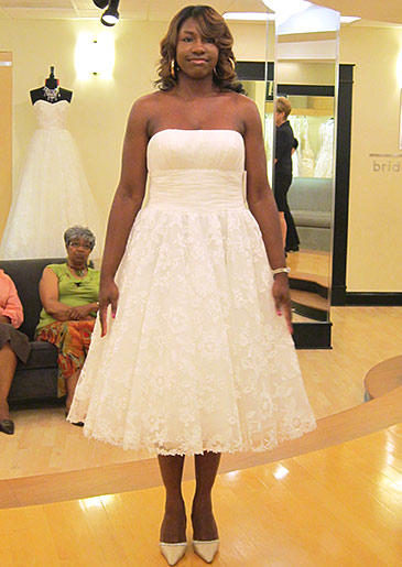 A tea-length gown with a lace skirt and banded waist is crowned with a simple straight neckline that balances the more elaborate hem.
