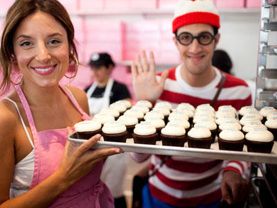 Katherine displays a tray of cupcakes while Waldo waves. Or maybe he's just waiting to snatch a cupcake?