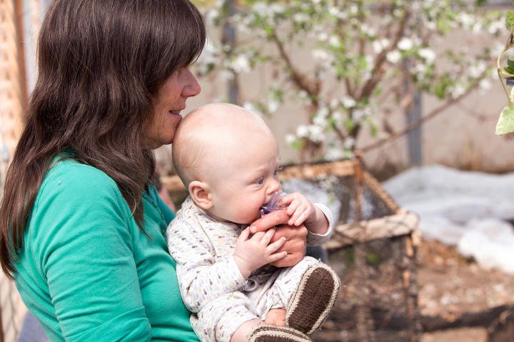 Grandmother Dena holding baby Findlay as Eve works to construct the playpen.