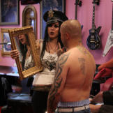 Through every step, Kat makes sure that the client is satisfied with the process. Here she holds up a mirror for Aaron to examine his newest piece, his daughters’ names, which she has completed on the back of his neck.,