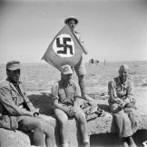 A British soldier in North Africa with his captured prizes of 3 Germans and a Nazi swastika flag, June 1942.