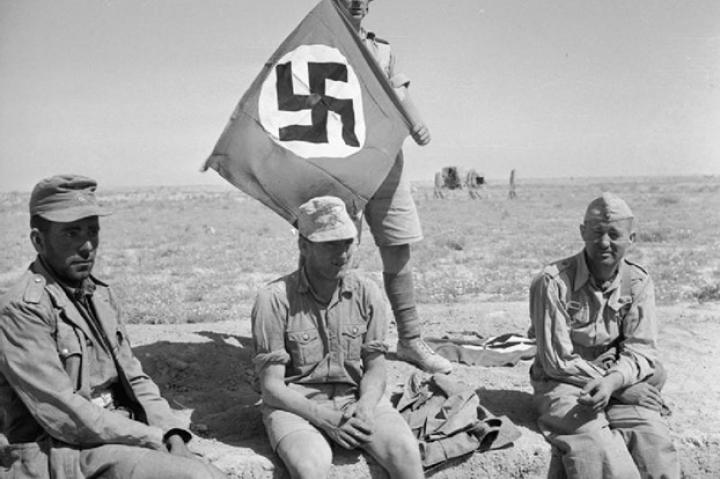 A British soldier in North Africa with his captured prizes of 3 Germans and a Nazi swastika flag, June 1942.