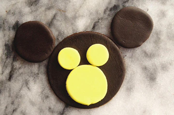 Using piping gel (or water), place the three yellow circles on the monkey face so that the larger circle is at the bottom of the cupcake and the two smaller yellow circles are equally spaced above the large yellow circle.