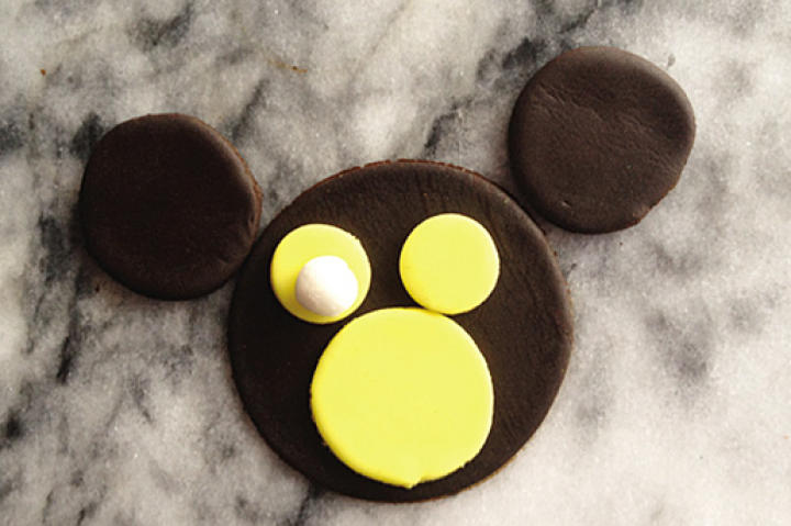 Also using piping gel to attach, place the white fondant balls on top of each of the smaller yellow circles to form the monkey’s eyes.