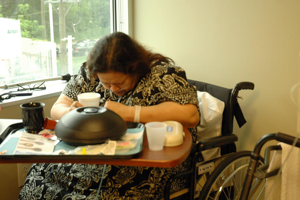 Olivia, still relying on oxygen for breathing, sits in her hospital room doubled over in pain.