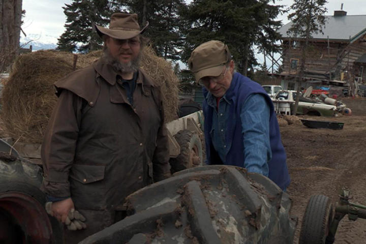Otto and Shane stands near a tractor and inspect the tires beofre heading out on the cattle drive.