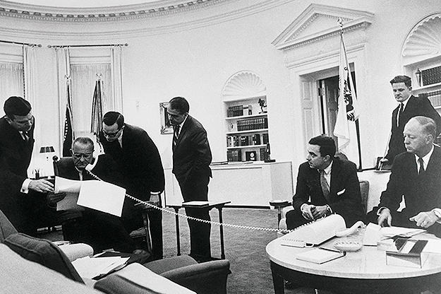A busy scene in President Johnson's White House office shows the chief executive and his aides laboring over the budget for fiscal 1967. They are, left to right, Marvin Watson, President Johnson, Press Secretary Bill Moyers, presidential assistants Jack Valenti and Joseph Califano, Budget Director Charles Schultze, and Deputy Budget Director Elmer B. Staats.