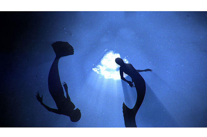 Mermaids swimming through the deep ocean.