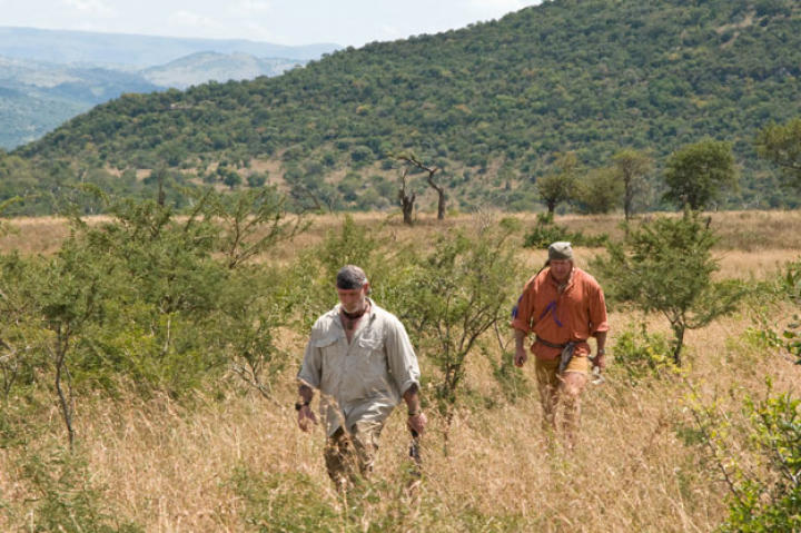 The survival duo starts out across the bush with all their senses on high alert. It's best to create a rapidly alternating rhythm of looking down — to avoid holes and snakes — and looking around to check for four-legged threats.