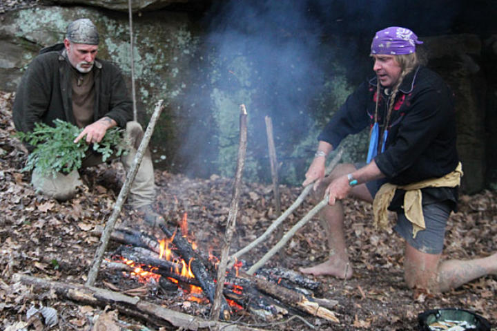 At their first campsite, Cody uses homemade fire tongs to grab a hot rock that he'll drop into the helmet stew pot (lower right). Boiling water with red hot rocks is a great way to both cook and sterilize water. Before dropping the stones in the water, you can brush off ash with green branches but everything that gets boiled will be clean even it's a little smutty.
