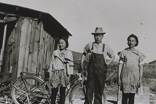 In this 1932 photograph, young John Schnabel and sisters Margaret and Mary stand in front of the shack they grew up in outside of Klamath Falls, Oregon. The 12 by 16 ft building was for the women while John and his brothers stayed in the chicken coop.