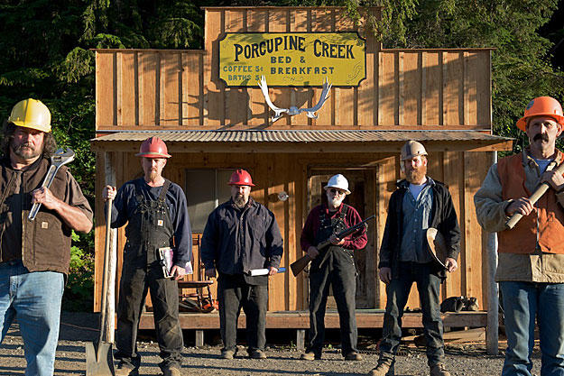The miners take their stand in front of their Porcupine Creek headquarters, built shortly after they first took possession of their claim. As a tribute to the first generation of miners who came to Porcupine Creek in the late 1890's, the 21st century crew put up a sign offering the going rate for coffee and a bath over century ago.