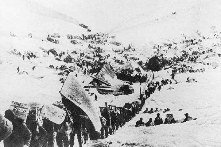 A line of prospectors begin their ascent toward the Chilkoot Pass that will take them over the border into Canada. Heavy snows in the fall of 1897 did little to stem the tide of fortune-seekers. Most of the arrivals were ill-prepared for what lay ahead as suggested by the fellow carrying a canoe on his back. Another carries a cumbersome crate labeled "Dyea" for the Alaskan town where many picked up supplies before heading out.
Few of the thousands who set out had any skill at gold prospecting. Likewise, hardly any carried sufficient supplies so that over the next months the greatest danger facing the Klondike miners was famine.