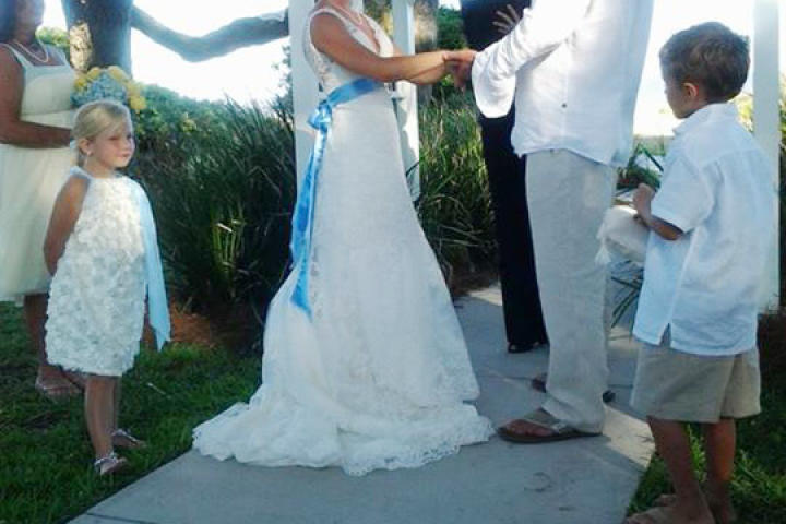 Ansley wears bright white lace, and her groom also wears light-colored attire for their beach wedding.