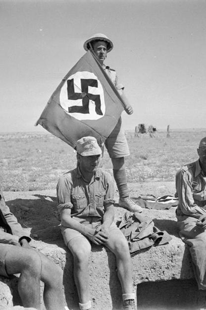 A British soldier in North Africa with his captured prizes of 3 Germans and a Nazi swastika flag, June 1942.