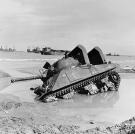 A stuck M4 Sherman tank on a Normandy invasion beach, June 12, 1944. Notice that the tank is fitted with raised air intakes for amphibious use.
Watch