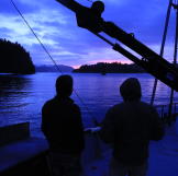 Two people admire the bold colors of the sunset on a boat.