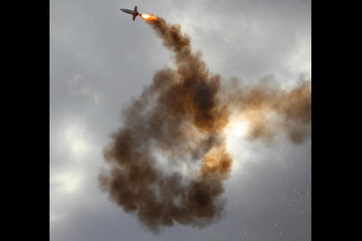 A rocket with dark tracking smoke against a cloudy sky.