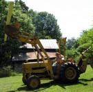 Tim drives a backhoe carrying beams for his new still house.