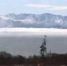 Snow capped mountains hang above the cloud line that covers the bay.