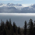Thick fog hangs over the far side of the bay and snow capped mountains.