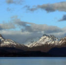 Mountians hovering over the waterline of the bay, as thick clouds move in from a fjord in the distance.[/br[