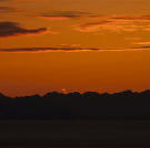 Looking across the bay at sunset, orange lines clouds hover over mountains across the bay.