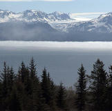 Thick fog hangs over the far side of the bay and snow capped mountains.