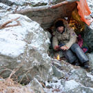 Les Stroud tries to keep warm under a makeshift shelter in the mountains.