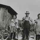 In this 1932 photograph, young John Schnabel and sisters Margaret and Mary stand in front of the shack they grew up in outside of Klamath Falls, Oregon. The 12 by 16 ft building was for the women while John and his brothers stayed in the chicken coop.
