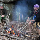 At their first campsite, Cody uses homemade fire tongs to grab a hot rock that he'll drop into the helmet stew pot (lower right). Boiling water with red hot rocks is a great way to both cook and sterilize water. Before dropping the stones in the water, you can brush off ash with green branches but everything that gets boiled will be clean even it's a little smutty.
