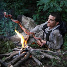 In Borneo, Bear Grylls grills a snake for dinner — but not before the non-venomous snake had bitten his hand.