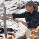 In Tasmania, Mykel uses a heavy rock as an assist while he splits a very hard piece of driftwood with his knife. Using even primitive tools, like this stone employed as a hammer, can save a lot of physical energy. Minimizing caloric expenditure is crucial when intake of food and water is so low.