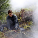 In New Zealand, after using his cell-phone battery to start a fire, Bear Grylls takes a minute to warm up.