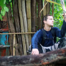 On an island in the Malay Archipelago Bear Grylls sits by his shelter, which he built from bamboo and bits of a broken-up boat. Not only does it protect him from the elements, but its roof is also capable of collecting rain water for drinking.