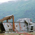 Todd stands with the massive shaker that was customized back at his airfield in Oregon and then transported to the claim. This vital piece of equipment was originally built to separate out different sizes of gravel using powerful side-to-side shaking motions and strategically-directed water jets.