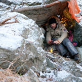 Les Stroud tries to keep warm under a makeshift shelter in the mountains.