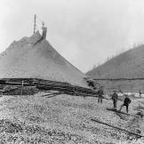 Miners stand next to a massive tailings pile in the heart of the Klondike gold fields. Moving and disposing of massive spoil piles demanded considerable time and labor.