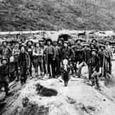 A group of miners employed by one of the Klondike's major claim holders pose with a young girl and a dog. Several years after the beginning of the gold rush, thousands of small claims were consolidated into fewer larger claims that could marshal the resources for mass processing and have some hope of turning a profit.