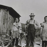 In this 1932 photograph, young John Schnabel and sisters Margaret and Mary stand in front of the shack they grew up in outside of Klamath Falls, Oregon. The 12 by 16 ft building was for the women while John and his brothers stayed in the chicken coop.