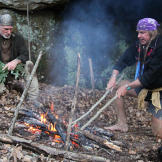 At their first campsite, Cody uses homemade fire tongs to grab a hot rock that he'll drop into the helmet stew pot (lower right). Boiling water with red hot rocks is a great way to both cook and sterilize water. Before dropping the stones in the water, you can brush off ash with green branches but everything that gets boiled will be clean even it's a little smutty.
