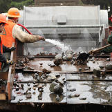 Jim Thurber and his crew work the larger tailings that have been separated out by the shaker. Removing these larger rocks is an unavoidable by-product of mass processing since the excavator's bucket picks up mixed loads. This requires more effort along the refinement chain but the expectation is for higher pay-outs that offset the extra work.