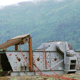 Todd stands with the massive shaker that was customized back at his airfield in Oregon and then transported to the claim. This vital piece of equipment was originally built to separate out different sizes of gravel using powerful side-to-side shaking motions and strategically-directed water jets.