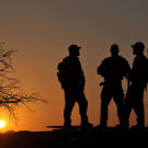 Rob (Navy SEAL ret.), Saw (Navy SEAL fmr.), Biggs (Navy SEAL fmr.), Oz (Green Beret) standing on Reva vehicle at dusk.