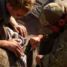 Saw (Navy SEAL fmr.) administering eye drops to rhino whilst being watched by pilot (Benjamin).